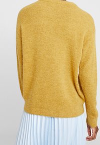 Suéter amarillo de punto con un acabado texturizado, que presenta un escote redondeado y un corte relajado. Combinado con una falda plisada de un azul claro.