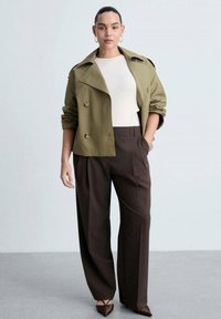 Olive green double-breasted jacket over a white top and brown wide-leg trousers. Brown pointed-toe shoes and hoop earrings complete the outfit.