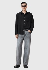 Sort, knap-op skjorte med en lomme; parret med let grå, løst siddende jeans; sorte støvler med rund tå; iført solbriller.