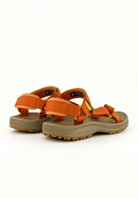Sandalias con tiras naranjas y amarillas, con una suela de goma beige texturizada y correas de velcro ajustables para estabilidad y comodidad.
