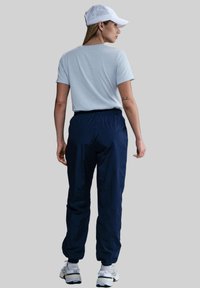 T-shirt azzurro chiaro, pantaloni navy con cintura elastica e berretto bianco. Il modello è di spalle, mostrando un abbigliamento sportivo casual.