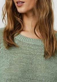 Maglione lavorato a maglia verde chiaro con scollatura rotonda, texture a trama larga e polsini a coste. Design semplice con dettagli ridotti al minimo.