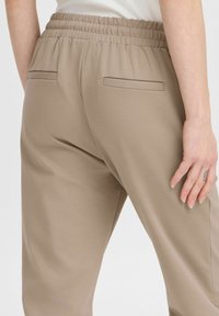 Beiga joggers med elastisk midja, med två passpojlösa fickor och en slät, mjuk tygkänsla. Passformen är avslappnad och bekväm.