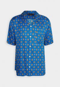 Chemise bleue à manches courtes, boutonnée, avec col et poche, présentant un motif répétitif de formes géométriques et florales multicolores.
