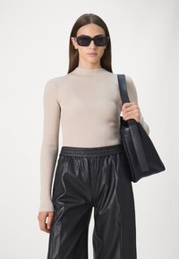 Beige ribaga pikkade varrukatega topp kõrge kaelusega, kombineeritud mustade nahast laia säärega pükstega. Mudel hoiab käes musta struktureeritud käekotti.