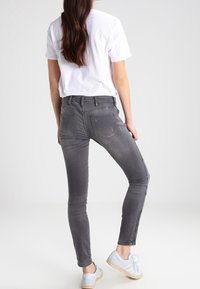 Hubené šedé džíny s vybledlým vzhledem, mají středně vysoký pas a zadní kapsy. V kombinaci s bílým tričkem a světle modrými teniskami.