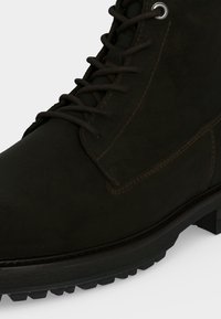 Κοντινό πλάνο ενός μαύρου μποτάκι με κορδόνια, πάτο από χοντρό καουτσούκ και ορατές ραφές στο πλάι και γύρω από την περιοχή των δαχτύλων.