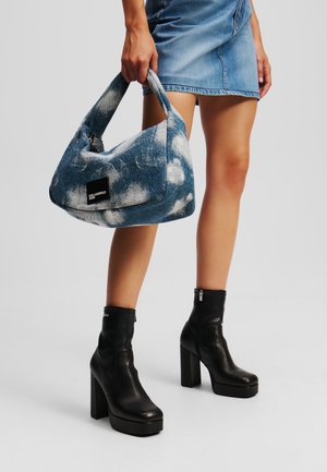 Borsa in denim blu con motivi a nuvola, grande forma hobo, texture morbida e un'etichetta logo nera. Abbinata a stivaletti neri con tacco.