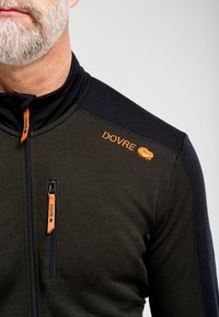 Mørkegrøn og marineblå lynlåsjakke med orange branding og lynlåstrækkere, høj krave og en tætsiddende pasform. Tekstureret stof.