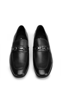 Mocasines negros con un diseño perforado en la parte frontal, detalles de cuero liso, punta cuadrada y adornos de hebilla metálica.