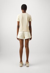 Camiseta de algodón beige con mangas cortas, combinada con pantalones cortos crema a juego. El modelo lleva zuecos de plataforma de color claro con acentos de madera.
