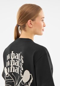 Černé oversized tričko s velkým bílým grafickým textem a designem na zadní straně, zobrazením stylizované ilustrace hmyzu.