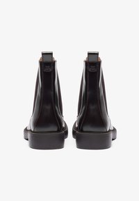 Rudi odiniai kulkšniniai batai su lygiąja apdaila, elastingais šonais ir kontrastingomis siūlėmis; plokščiais padais ir kilpelėmis gale.