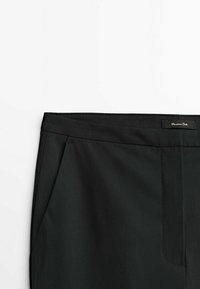 Svarta skräddarsydda byxor med sidofickor och en midja som har en liten sydd varumärkesetikett på högra sidan.