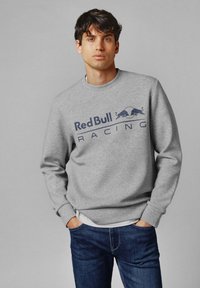 Sudadera gris con cuello redondo, que presenta un gráfico en azul marino de "Red Bull Racing" y dos imágenes estilizadas de toros. Combinada con vaqueros azules.