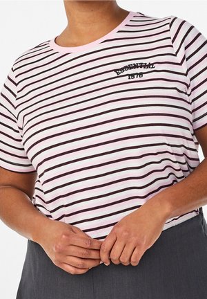 Personne portant une chemise rayée rose et blanche avec un texte noir "ESSENTIAL 1978" sur la poitrine, mains jointes près d'un pantalon gris foncé.