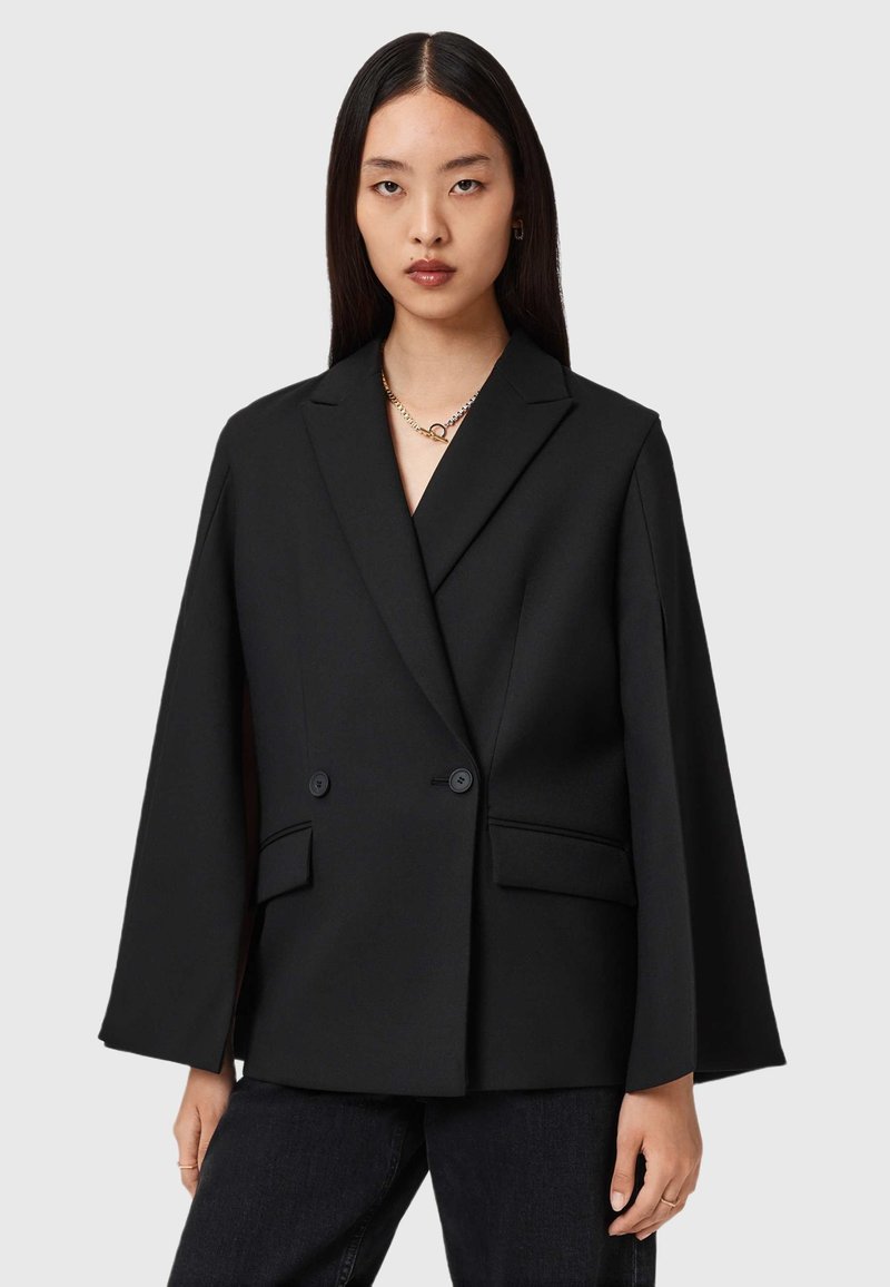 Blazer noir à double boutonnage avec des manches larges, coupe ajustée et revers crantés, comprenant deux poches avant et des accents en boutons.