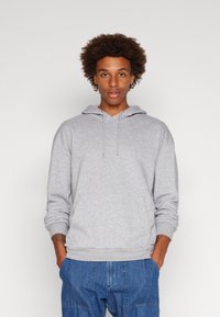 Lys grå hettegenser med snor i hetta, ribbestrikkede mansjetter og nederkant, laget av myk stoff, med en avslappet passform. Kombinert med blå denimbukser.
