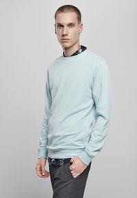 Hele sinine ujumispaita, millel on ümar kaelus ja pikad varrukad, millel on sile tekstuur. Kandmise all on tume mustriga särk ja hallad püksid.