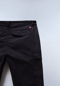 Πλάγια όψη μαύρου παντελονιού cargo με πλαϊνές και πίσω τσέπες με καπάκι, που διαθέτει μια μικρή ετικέτα με τη σημαία της Νορβηγίας κοντά στη μέση.