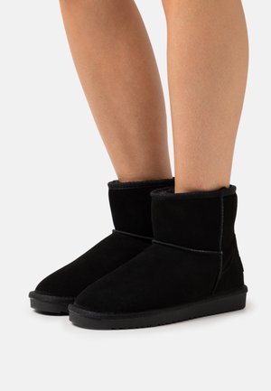 Schwarze Wildleder-Stiefeletten mit einem weichen Innenfutter, runder Spitze und flacher Gummisohle, die dekorative Nähte entlang der Nähte aufweisen.