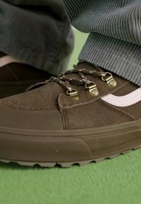 Zapatillas de ante marrón con suela de goma, que presentan ojales de metal, cordones marrones y una franja lateral blanca. Tela texturizada y cordones planos.