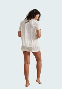 Korte mouwen, lichtgekleurde pyjama set met gestreept ontwerp. De top heeft een ontspannen pasvorm, en de shorts zijn vergelijkbaar gestyled met accenten aan de randen.