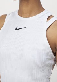 Gros plan sur une personne portant un haut sans manches Nike blanc à côtes avec de fines bretelles et un logo Nike noir sur la poitrine.