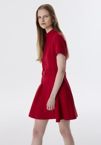 Abito rosso a maniche corte con colletto alto, cintura in vita e gonna a ruota. Realizzato in tessuto liscio con linee pulite e dettagli minimi.