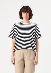 Tricou în dungi, cu nuanțe de bleumarin și alb, cu mâneci scurte, guler rotund, croială lejeră, asociat cu pantaloni bej cu talie înaltă, textură de țesătură netedă.