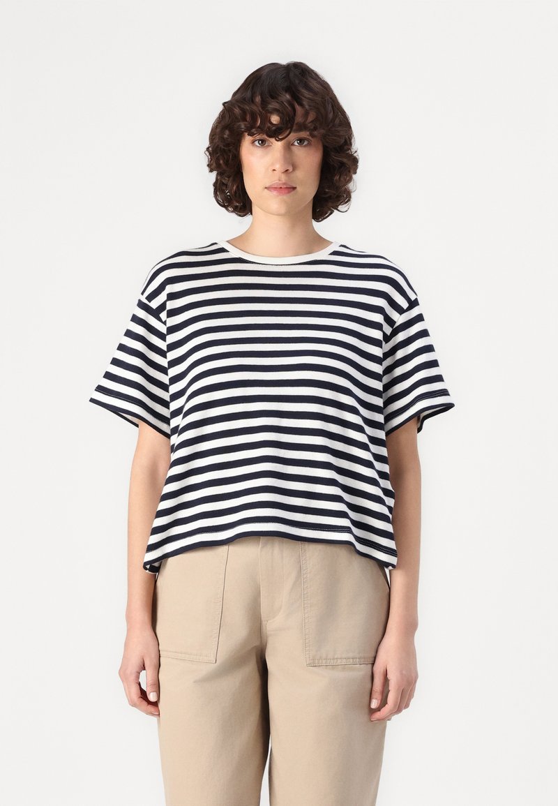 Tricou în dungi, cu nuanțe de bleumarin și alb, cu mâneci scurte, guler rotund, croială lejeră, asociat cu pantaloni bej cu talie înaltă, textură de țesătură netedă.