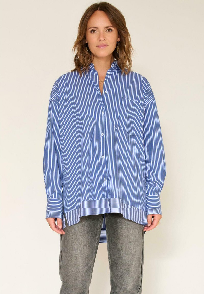 Chemise à rayures bleues et blanches, à boutons, avec un col, une poche poitrine et des manches longues. Bande rayée plus claire au niveau de l'ourlet et des poignets.