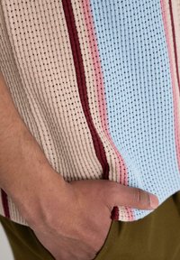Knit top with vertical stripes in blue, beige, pink, and burgundy. Features a textured, breathable fabric with a loose fit.