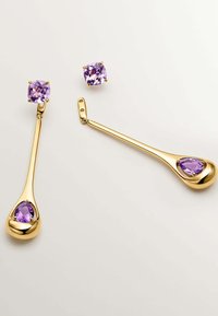 Pendientes en tono dorado con un dise ño de gota que presenta una piedra morada en forma de pera, complementados por un pendiente de botón cuadrado morado.