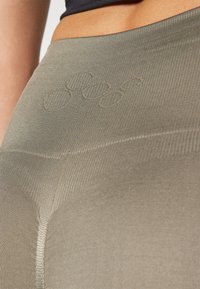 Leggings vert olive avec texture côtelée, ornés de broderies circulaires discrètes. Design ajusté avec une taille mi-haute.