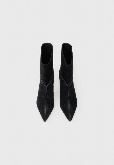 Schwarze Wildleder-Stiefeletten mit spitzen Zehen, die kontrastierende weiße Nähte an den Seiten und eine schmale Silhouette aufweisen.