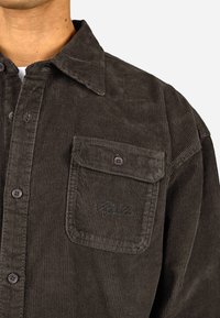 Barna kordbársony ing, gombos gallérral, elülső zseb embroidered részletekkel és műanyag gombokkal. Texturált anyag függőleges csíkokkal.