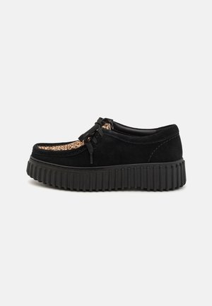 Czarne zamszowe buty z akcentem w panterkę, okrągły czubek, sznurowany design oraz gruba czarna gumowa podeszwa z ryflowanym wzorem.