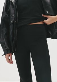 Sort læderjakke med struktureret overflade, b�året over en tætsiddende sort top og slanke sorte bukser, der fremhæver et monokrom look.