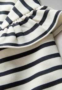 Tela a rayas en crema y azul marino, con un dobladillo con volantes y una textura suave. Las rayas están espaciadas uniformemente, creando un aspecto clásico.