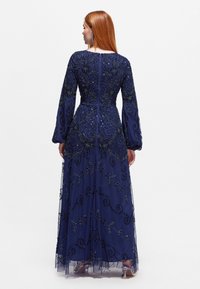 Námorně modré šaty s dlouhými rukávy, zdobené složitým korálkováním a květinovou výšivkou. Průsvitná vrstva s volnou sukní a přiléhavým živůtkem.