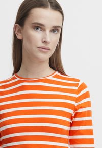 Orange- och vitrandig långärmad topp med rund halsringning, tillverkad av ett slätt tyg, med jämnt fördelade horisontella ränder.