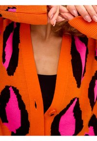 Orange cardigan with a bold leopard print in black and bright pink. Features a V-neck, button closure, and textured knit material.