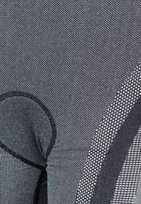 Svart nät tyg med ett texturerat mönster, en cirkulär utskärning och kontrasterande släta linjer. Hållbara och ventilerande designelement.