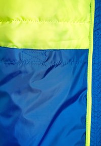 Zbliżenie niebieskiego i neonowo-żółtego materiału z dokładnym szyciem, prawdopodobnie część kurtki lub odzieży na świeżym powietrzu.