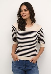 Maglione a righe beige chiaro e navy con scollatura rotonda, maniche corte a palloncino e orlo aderente, indossato con jeans blu.
