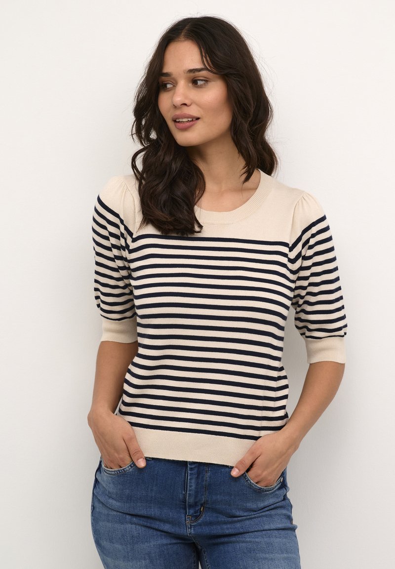 Maglione a righe beige chiaro e navy con scollatura rotonda, maniche corte a palloncino e orlo aderente, indossato con jeans blu.