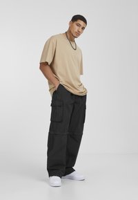 Beige oversized t-shirt, zwarte cargobroek met meerdere zakken, gestructureerde stof, gecombineerd met witte sneakers, minimalistisch ontwerp, neutrale kleuren.