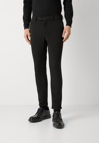 Black slim-fit trousers with a smooth texture, featuring a button closure, belt loops, and rolled cuffs, paired with black lace-up shoes.