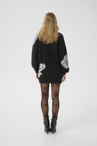 Zwart sweater met oversized mouwen met tonale rozenpatronen, gecombineerd met een zwarte minirok en kousen met een bloempatroon. Chunky haklaarzen.